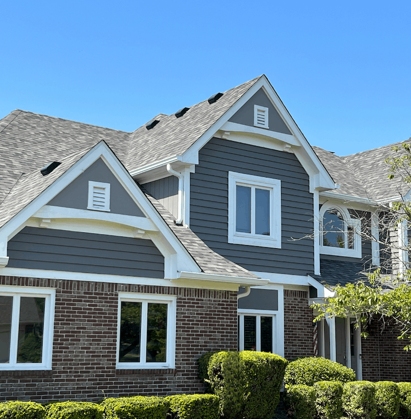 Avon Indiana Roofing Contractor — Gray Shingles on Brick Home Front view of a two-story brick home in Avon Indiana with a completed roof replacement featuring charcoal architectural shingles and new gutters by Robert Stevens Roofing
