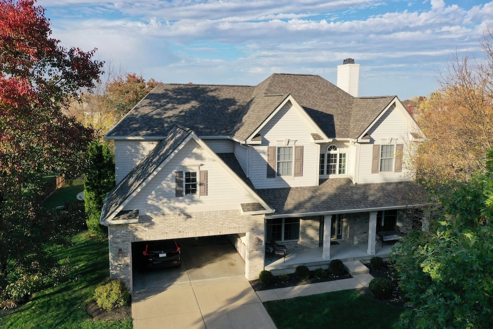 Aerial view of a large two-story brick home with completed gray architectural shingle roof replacement and chimney in Zionsville, Indiana by Robert Stevens Roofing