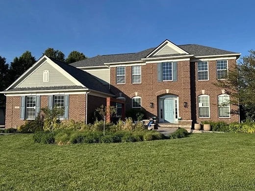 Large two-story brick home with charcoal asphalt shingle roof and blue shutters in Zionsville, Indiana, by Robert Stevens Roofing
